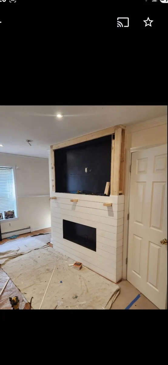 Unfinished shiplap fireplace and media wall framed in raw wood with drop cloths on the floor