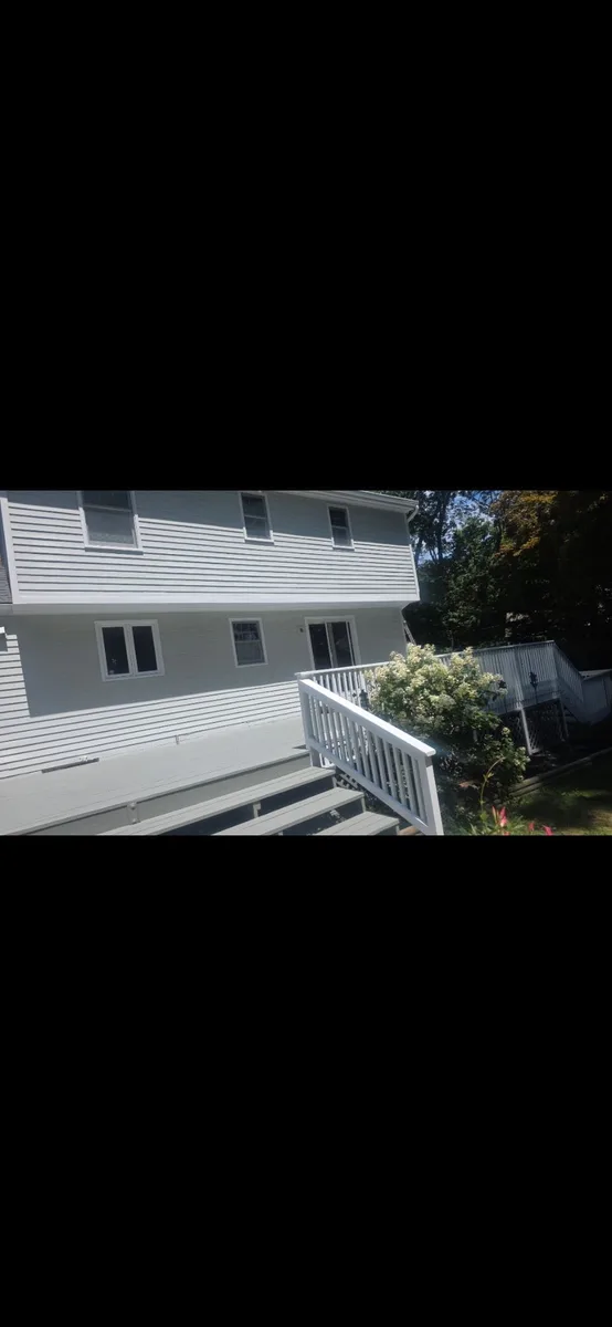 Freshly painted light siding with a refreshed deck and white railing at the rear of a home