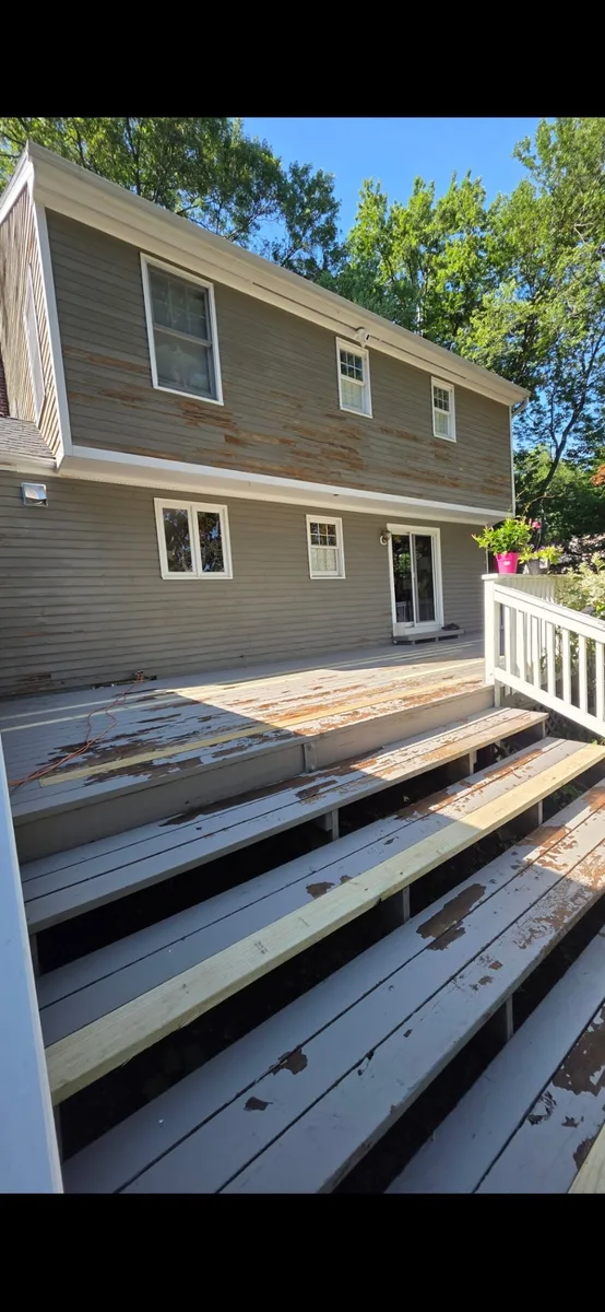 Rear of a gray-sided home with peeling paint across the siding and worn deck boards